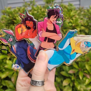 May include: A collection of colorful acrylic keychains featuring anime-style illustrations. The keychains depict various characters in dynamic poses, with vibrant colors and detailed designs. The characters include a bat-like figure, a red-skinned woman, and two other female figures.