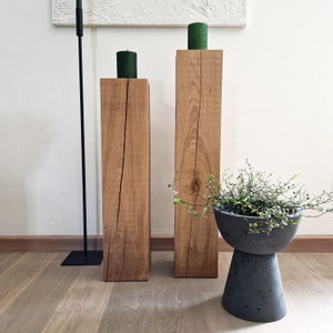 May include: Two wooden candle holders with a natural wood finish and a crack running down the center of each. The candle holders are on a light wood floor. A small potted plant is in the foreground.