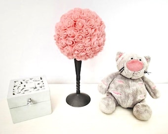 May include: A pink rose ball centerpiece on a black stand, a gray plush cat toy with pink accents, and a white decorative box with a floral design.