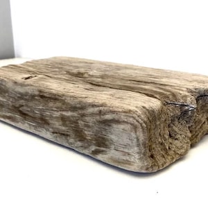 Può includere: Un pezzo di legno di deriva con un aspetto naturale e rustico. Il legno ha un colore marrone chiaro con striature grigie e bianche. Ha una superficie ruvida e testurizzata ed è di forma rettangolare.