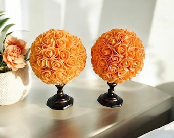 May include: Two orange rose sphere arrangements on black pedestals. The spheres are made of many small, individual roses.
