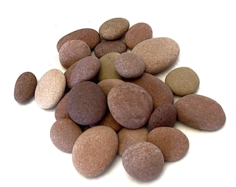 May include: A collection of smooth, oval-shaped stones in shades of brown, beige, and reddish-brown. The stones are arranged in a pile, with some overlapping.