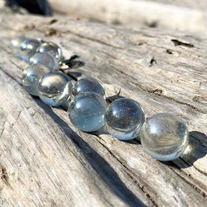 Puede incluir: Una fila de canicas de vidrio transparente sobre una superficie de madera desgastada. Las canicas están dispuestas en una línea curva, con la canica más grande en el centro.