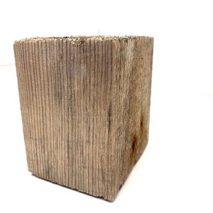Op de afbeelding: Een verweerd, rechthoekig blok hout met een ruw, getextureerd oppervlak. Het hout heeft een natuurlijke, lichtbruine kleur met donkerdere strepen en knopen.
