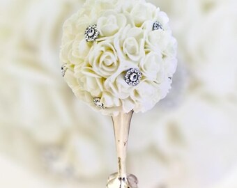 May include: A white flower ball with rhinestones on a silver stand. The flower ball is made of small white roses.