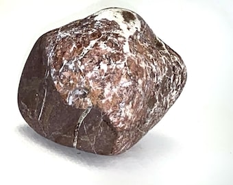 Può includere: Una pietra liscia e arrotondata caratterizzata da una superficie maculata con toni marrone rossastro intenso e marrone scuro, accentuata da venature e macchie minerali bianche irregolari che creano un aspetto testurizzato e marmorizzato.