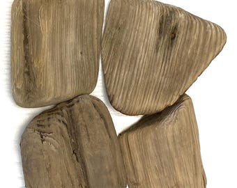 Puede incluir: Cuatro piezas de madera flotante desgastada con un tono marrón claro grisáceo. Cada pieza muestra una textura de grano de madera natural distinta con bordes suaves y redondeados y formas irregulares, exhibiendo el aspecto orgánico de la madera.