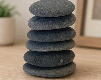 Può includere: Una pila verticale di sei ciottoli di fiume grigio scuro, lisci e di forma ovale. Ogni pietra è appiattita ed equilibrata una sopra l'altra per formare una colonna singola. La consistenza delle pietre appare opaca e uniforme, con sfumature.
