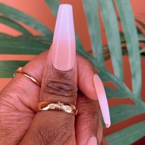 May include: Close-up of a hand with long, light pink and white ombre nails. The nails are long and almond shaped.