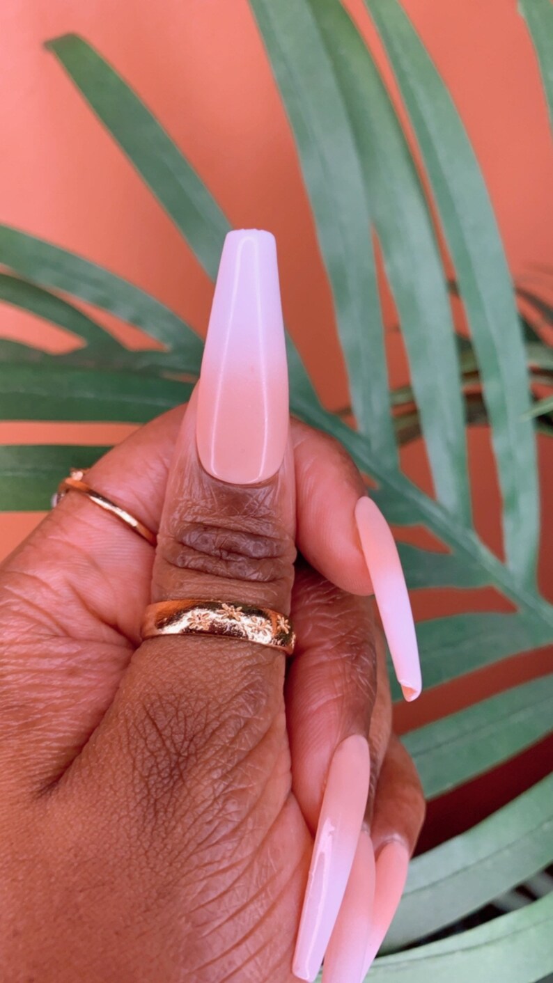 May include: Close-up of a hand with long, light pink and white ombre nails. The nails are long and almond shaped.