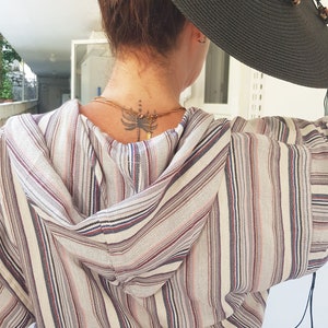 May include: A striped hooded dress with a white background and thin stripes of pink, blue, and black. The dress has a drawstring waist and a hood. The person is wearing a large black sun hat.