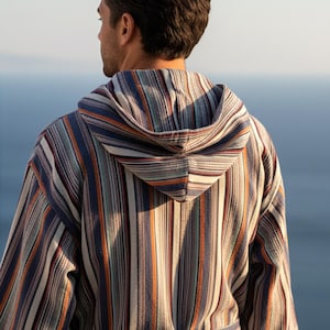 May include: A hooded bathrobe featuring a vertical striped pattern in shades of navy blue, white, orange, and light blue. The garment includes long sleeves, a hood, and a matching fabric belt tied around the waist, showcasing a textured weave.