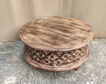 May include: A round wooden stool with a carved design around the base. The stool is dark brown and has a distressed finish.