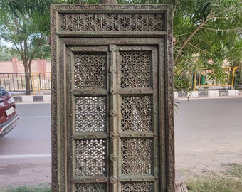 May include: A large, intricately carved wooden door with a green patina. The door is made of multiple panels with a lattice design and features decorative details around the frame.