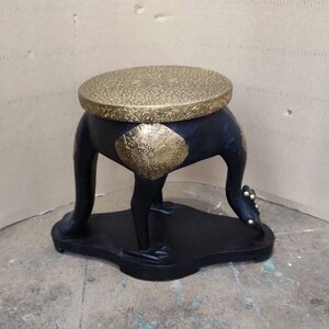 May include: A black wooden stool with gold accents shaped like a bird. The stool has a round top and three legs.
