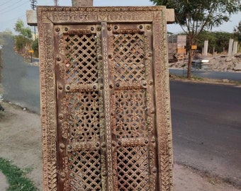 May include: A vintage wooden windowpane with intricate carvings and a lattice design. The windowpane is painted in a light brown colour and has a distressed look. It is framed with a thick wooden border.