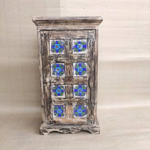 May include: A small wooden cabinet with a distressed white finish. The cabinet door is decorated with blue and green floral tiles.