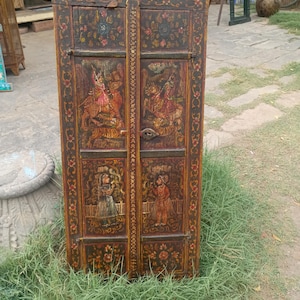 Puede incluir: Una puerta de armario rectangular de madera marrón oscura con detalles pintados a mano en rojo, amarillo y verde. La superficie muestra intrincados bordes florales y cuatro paneles que representan figuras a caballo y personas de pie con vestimenta tradicional.