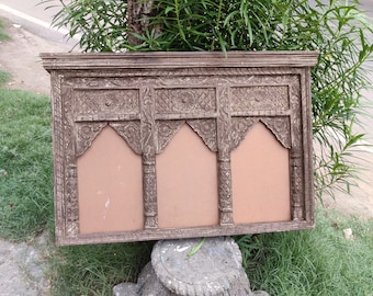 Può includere: Una cornice in legno marrone con intagli intricati e tre aperture ad arco. La cornice poggia su una base in pietra.