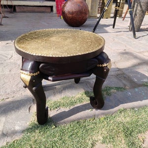 May include: A round, wooden table with a brass top and elephant-shaped legs. The table is dark brown with gold accents.