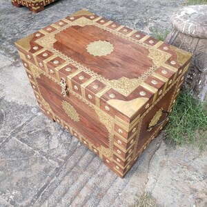 May include: A wooden chest with intricate brass inlay designs. The chest has a dark brown finish and features a brass handle on the side.