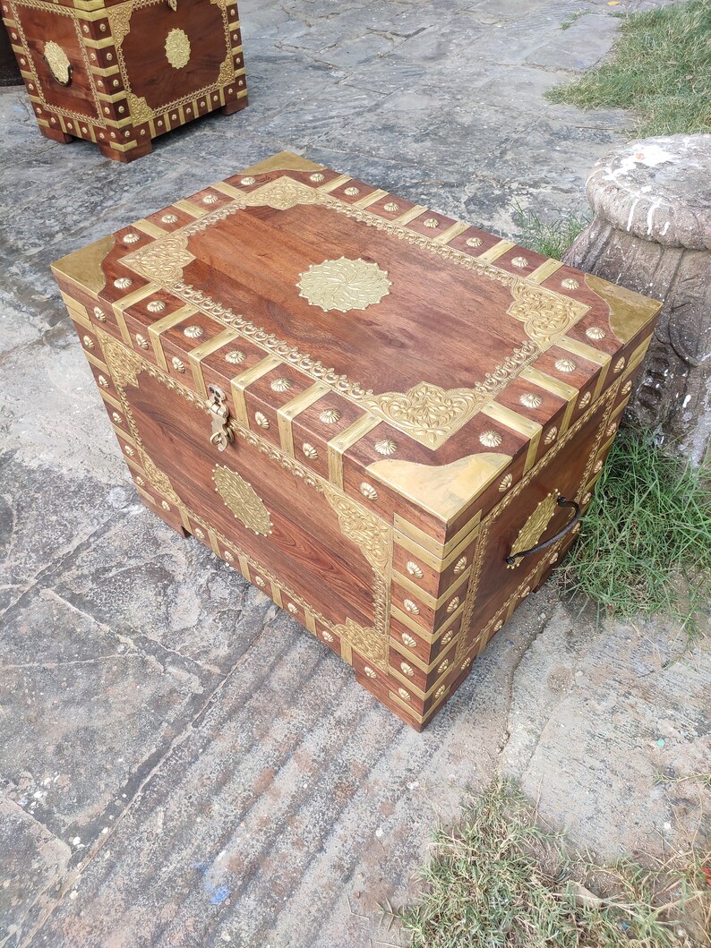 May include: A wooden chest with intricate brass inlay designs. The chest has a dark brown finish and features a brass handle on the side.