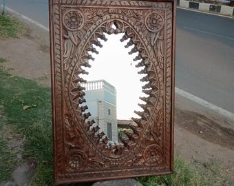 May include: A brown wooden mirror with intricate carvings around the oval-shaped glass. The mirror is leaning against a stone base.
