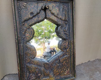 May include: A carved wooden mirror with a green, black, and gold paint finish. The mirror has an intricate design with a central arched opening.