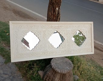 Può includere: Specchio in legno bianco intagliato con tre specchi rettangolari. Lo specchio è appoggiato a un tronco d'albero.