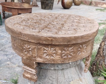 May include: A round wooden stool with intricate carvings and a dark brown finish. The stool has three legs and a decorative design around the top edge.