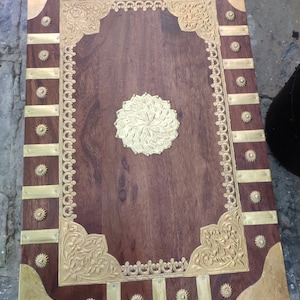 May include: A wooden box with a decorative brass inlay. The box has a dark brown wood finish and a brass border with intricate floral designs. The top of the box features a large brass circle with a floral design.