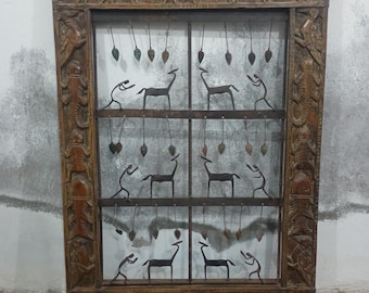 Puede incluir: Una pieza de arte mural con marco de madera con figuras de animales talladas y un diseño de rejilla metálica. El marco es de color marrón cálido, y la rejilla presenta ciervos y figuras humanas estilizadas. Elementos decorativos cuelgan de la parte superior.