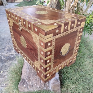 May include: A wooden chest with intricate brass accents and a decorative brass handle. The chest is decorated with floral patterns and has a dark brown finish.