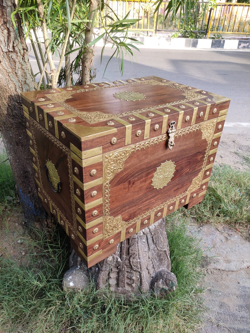 May include: A wooden chest with brass accents and intricate carvings. The chest has a hinged lid and a brass lock. The chest is sitting on a tree stump.