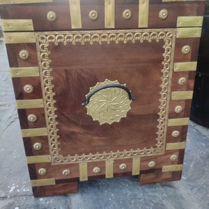 May include: A wooden chest with gold accents and a black metal handle. The chest has a decorative design around the edges and a floral pattern on the front.