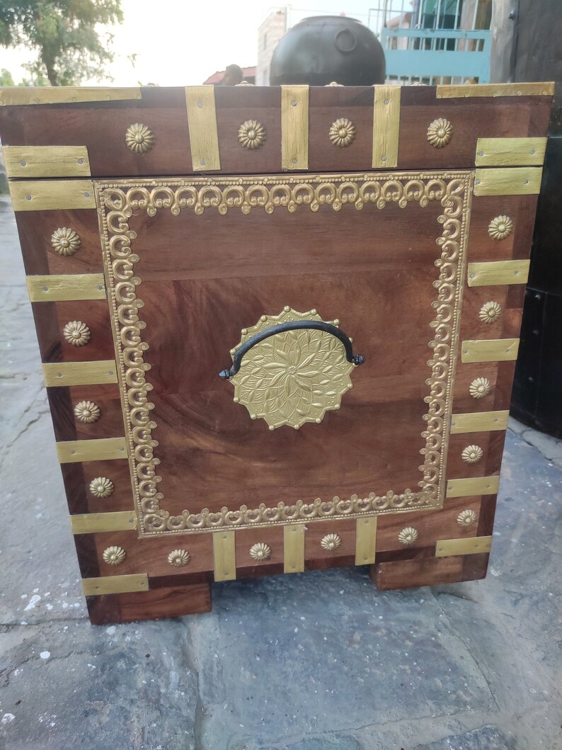 May include: A wooden chest with gold accents and a black metal handle. The chest has a decorative design around the edges and a floral pattern on the front.