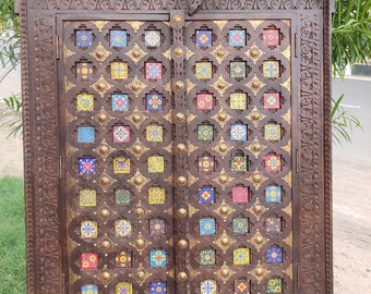 Puede incluir: Un armario de madera marrón oscuro con dos puertas. Las puertas están decoradas con intrincados tallados e incrustadas con azulejos coloridos. El armario tiene un diseño tradicional indio.