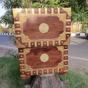 May include: Two wooden boxes with intricate brass inlays. The boxes are stacked on top of each other and have a dark brown finish. The brass inlays feature a floral design and a circular motif in the center.