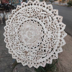 May include: White wooden wall decor with intricate carved floral patterns. The design features a large central flower surrounded by smaller floral motifs.