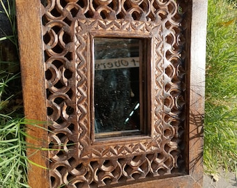 May include: A rectangular wooden mirror with intricate carved details around the frame. The mirror has a dark brown finish and a simple rectangular shape.