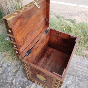 May include: A wooden storage chest with a hinged lid and brass accents. The chest is open and the interior is visible. The chest has a decorative brass handle on the front.
