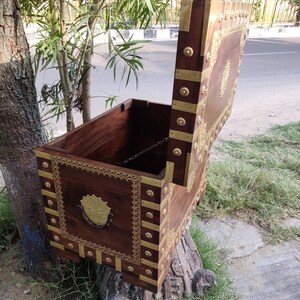 May include: A wooden chest with a hinged lid, decorated with brass accents and intricate carvings. The chest is open, revealing the interior.