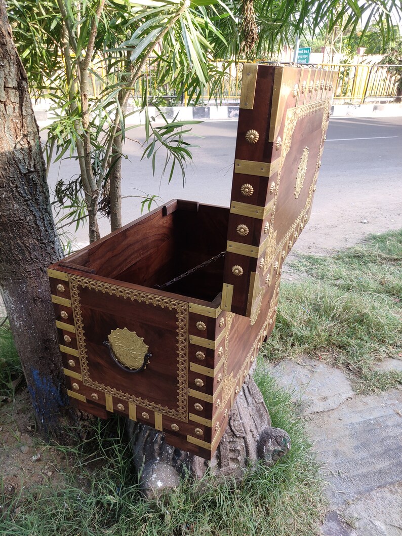 May include: A wooden chest with a hinged lid, decorated with brass accents and intricate carvings. The chest is open, revealing the interior.