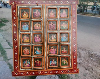 Puede incluir: Un panel decorativo enmarcado en madera con un borde rojo y naranja. El panel está dividido en 24 cuadrados, cada uno con una imagen pintada de una persona con ropa tradicional. El panel está decorado con pequeñas cuentas blancas y diseños florales.
