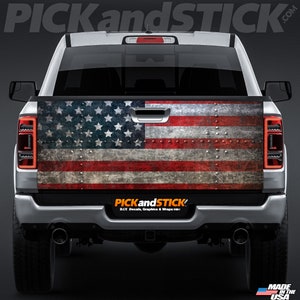 May include: A silver pickup truck with a distressed American flag decal on the tailgate. The decal features a weathered, rusty look with rivets.