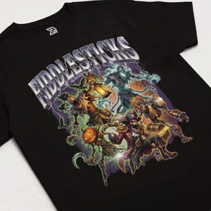 May include: Black t-shirt featuring a colorful graphic of several fantasy characters, including a pirate, a scarecrow, and a robot. The word "FIDDLESTICKS" is printed across the top in a silver, stylized font. The design is set against a backdrop of purple lightning.