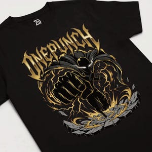 Può includere: T-shirt nera con grafica oro e nera di un supereroe che colpisce. Il design include il testo "ONE PUNCH" in oro, con un'illustrazione dinamica di una figura circondata da fulmini e che rompe la pietra.
