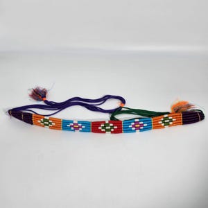 May include: A colorful woven belt with a geometric pattern in shades of orange, red, blue, green, and purple. The belt has two long ties on either end.
