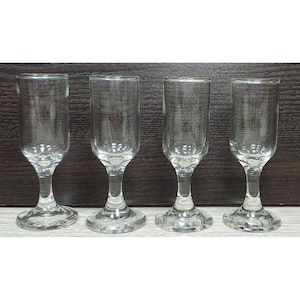 Puede incluir: Un juego de cuatro copas de licor de cristal transparente, cada una con un cuenco cilíndrico alto, un tallo corto y grueso, y una base circular ancha y estable. Las copas son transparentes y tienen un acabado liso y pulido, diseñadas para servir pequeñas porciones de licores.
