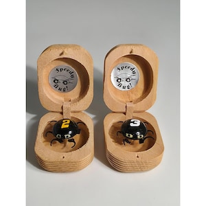 May include: Two light-colored wooden cases, each containing a small black bug-shaped toy. The left bug features a yellow number 2, and the right bug features a white number 3. Each case lid displays a silver circular sticker with the text Speedy Bug!